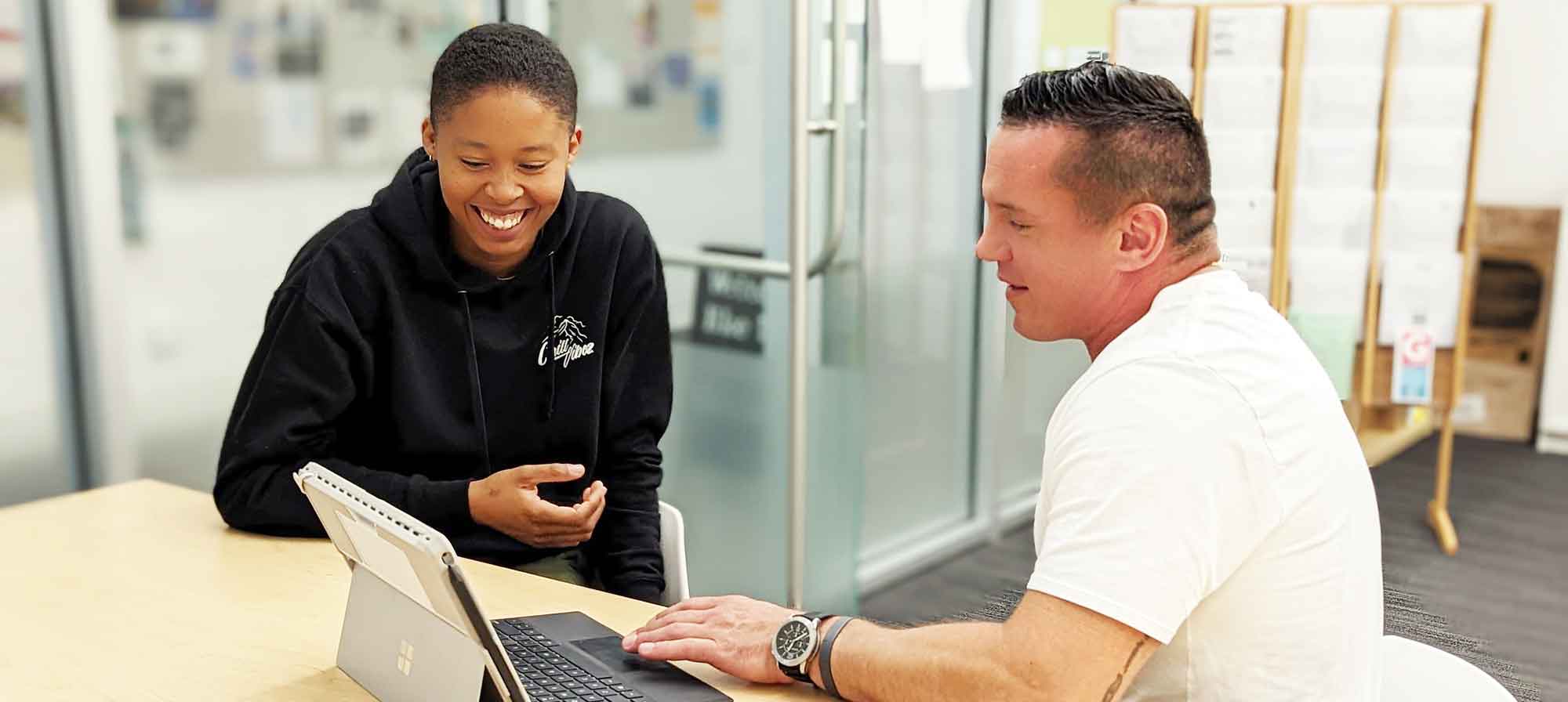 Two students are sitting in the Writing Center conference room, working on a tablet computer together.