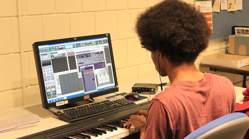 A student uses a computer and keyboard workstation to work on a musical composition
