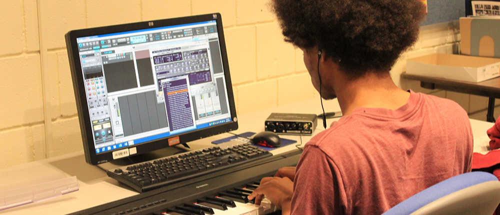 A student uses a computer and keyboard workstation to work on a musical composition